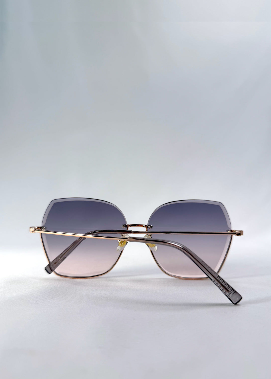Folded view of Aureon sunglasses in Rosé Quartz, featuring rimless metal frame, pale metal temples, and pink-grey gradient lenses, showing the folded temples and frame profile. 