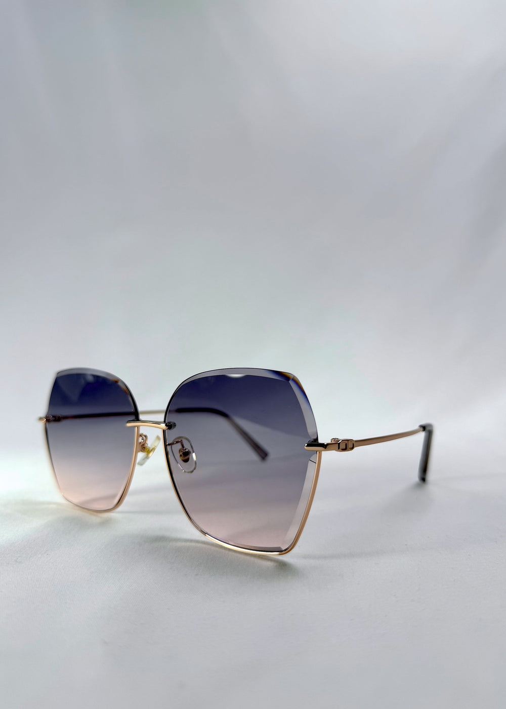 Three-quarter front view of Aureon sunglasses in Rosé Quartz, featuring rimless metal frame, pale metal temples, and pink-grey gradient lenses, showing the front shape and temple profile. #color_ros-quartz