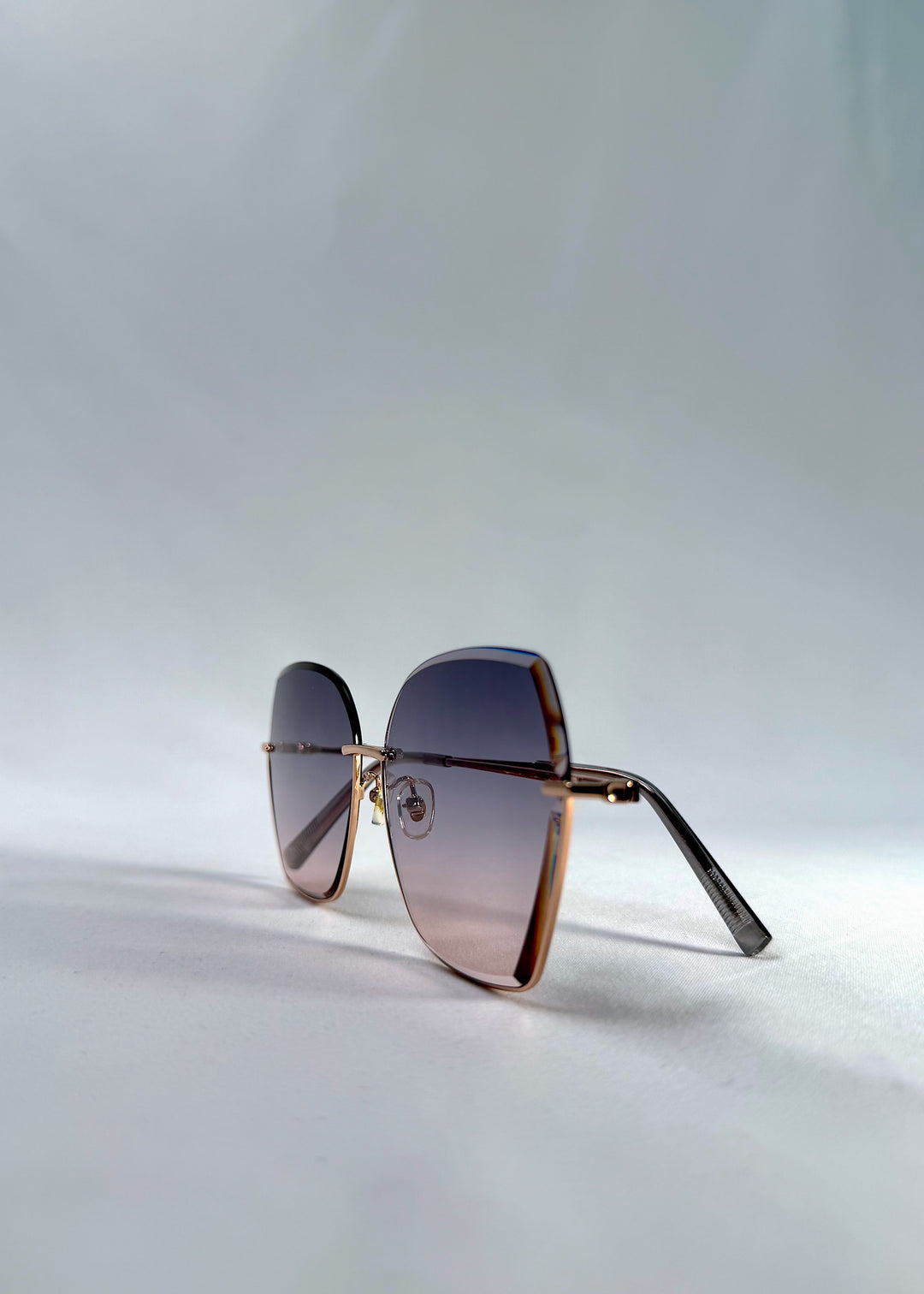 Side-angle view of Aureon sunglasses in Rosé Quartz, featuring rimless metal frame, pale metal temples, and pink-grey gradient lenses, showing the angled side profile and lens depth.