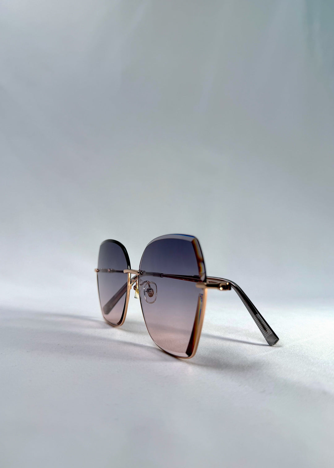 Side-angle view of Aureon sunglasses in Rosé Quartz, featuring rimless metal frame, pale metal temples, and pink-grey gradient lenses, showing the angled side profile and lens depth. 