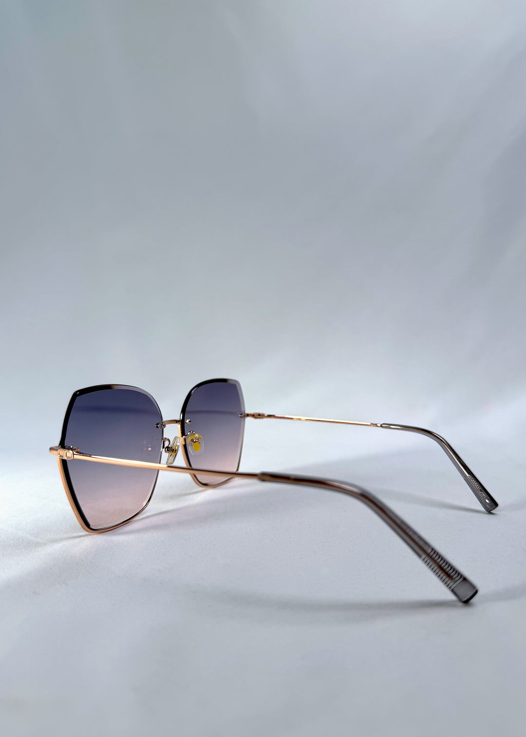 Side view of Aureon sunglasses in Rosé Quartz, featuring rimless metal frame, pale metal temples, and pink-grey gradient lenses, showing the lens shape and temple profile.