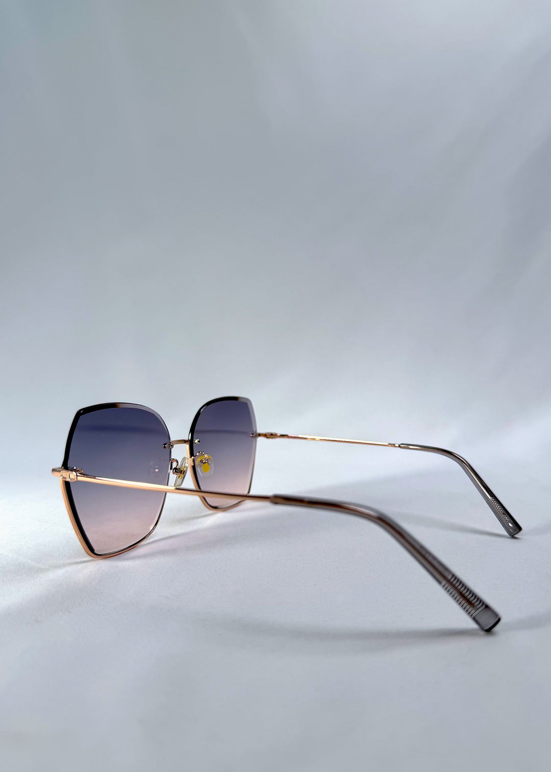 Side view of Aureon sunglasses in Rosé Quartz, featuring rimless metal frame, pale metal temples, and pink-grey gradient lenses, showing the lens shape and temple profile. 