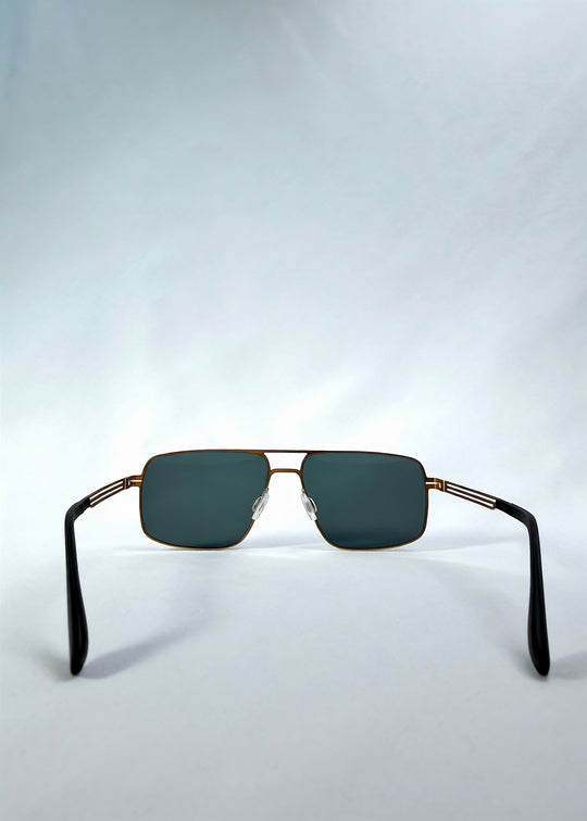 Back view of Axiom sunglasses in Antique Brass, featuring antique brass rectangular metal frame and green-grey polarized lenses, showing the inside frame and open temples.