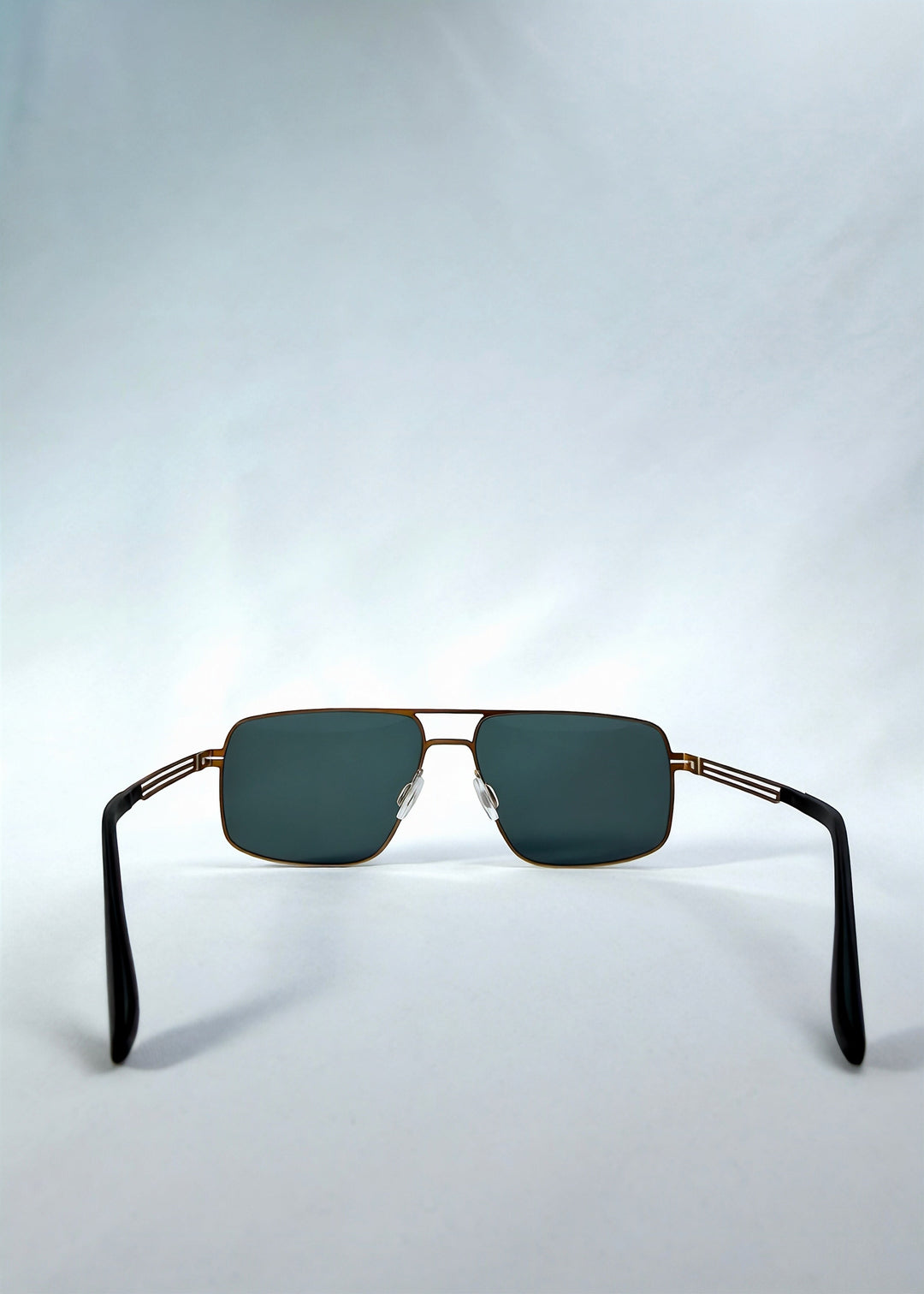 Back view of Axiom sunglasses in Antique Brass, featuring antique brass rectangular metal frame and green-grey polarized lenses, showing the inside frame and open temples. 