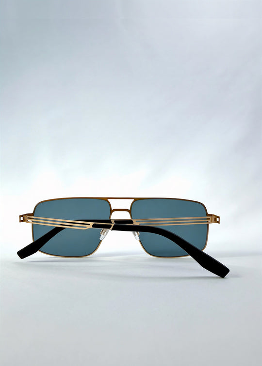 Folded view of Axiom sunglasses in Antique Brass, featuring antique brass rectangular metal frame and green-grey polarized lenses, showing the folded temples and frame profile. 