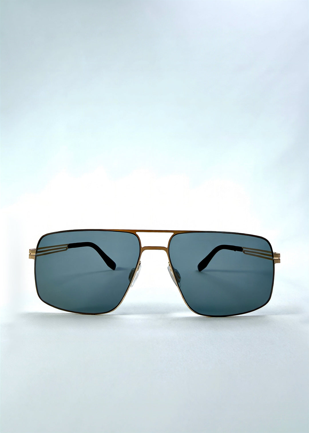 Front view of Axiom sunglasses in Antique Brass, featuring antique brass rectangular metal frame and green-grey polarized lenses, showing the full front silhouette. 