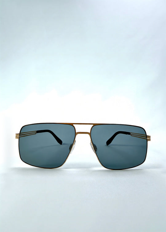 Front view of Axiom sunglasses in Antique Brass, featuring antique brass rectangular metal frame and green-grey polarized lenses, showing the full front silhouette. 