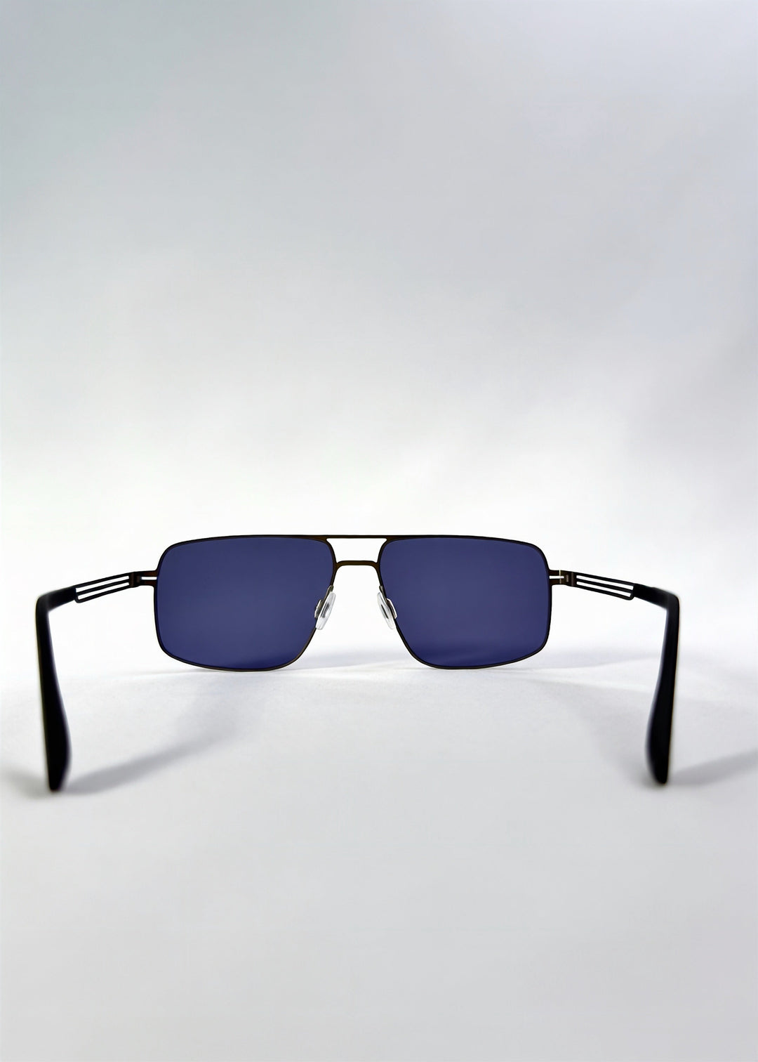 Back view of Axiom sunglasses in Blue Graphite, featuring blue-graphite rectangular metal frame and blue tinted polarized lenses, showing the inside frame and open temples. 