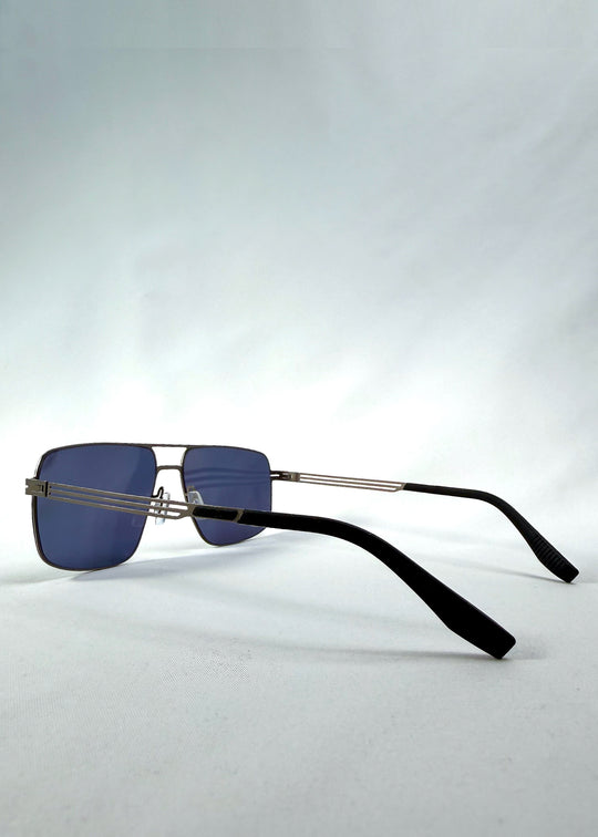 Three-quarter front view of Axiom sunglasses in Blue Graphite, featuring blue-graphite rectangular metal frame and blue tinted polarized lenses, showing the front shape and temple profile.