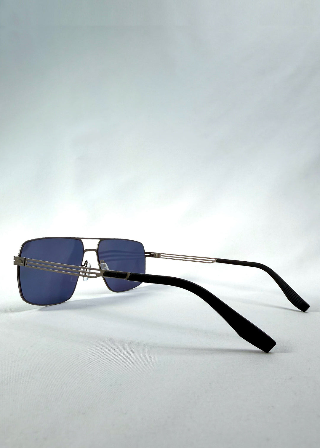 Three-quarter front view of Axiom sunglasses in Blue Graphite, featuring blue-graphite rectangular metal frame and blue tinted polarized lenses, showing the front shape and temple profile. 
