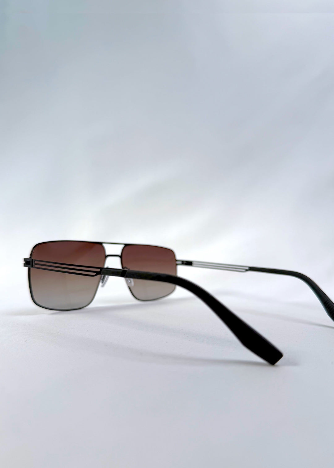 Back-angle view of Axiom sunglasses in Eclipse Black, featuring dark rectangular metal frame and shadowed gradient polarized lenses, showing the back structure and temple alignment. 