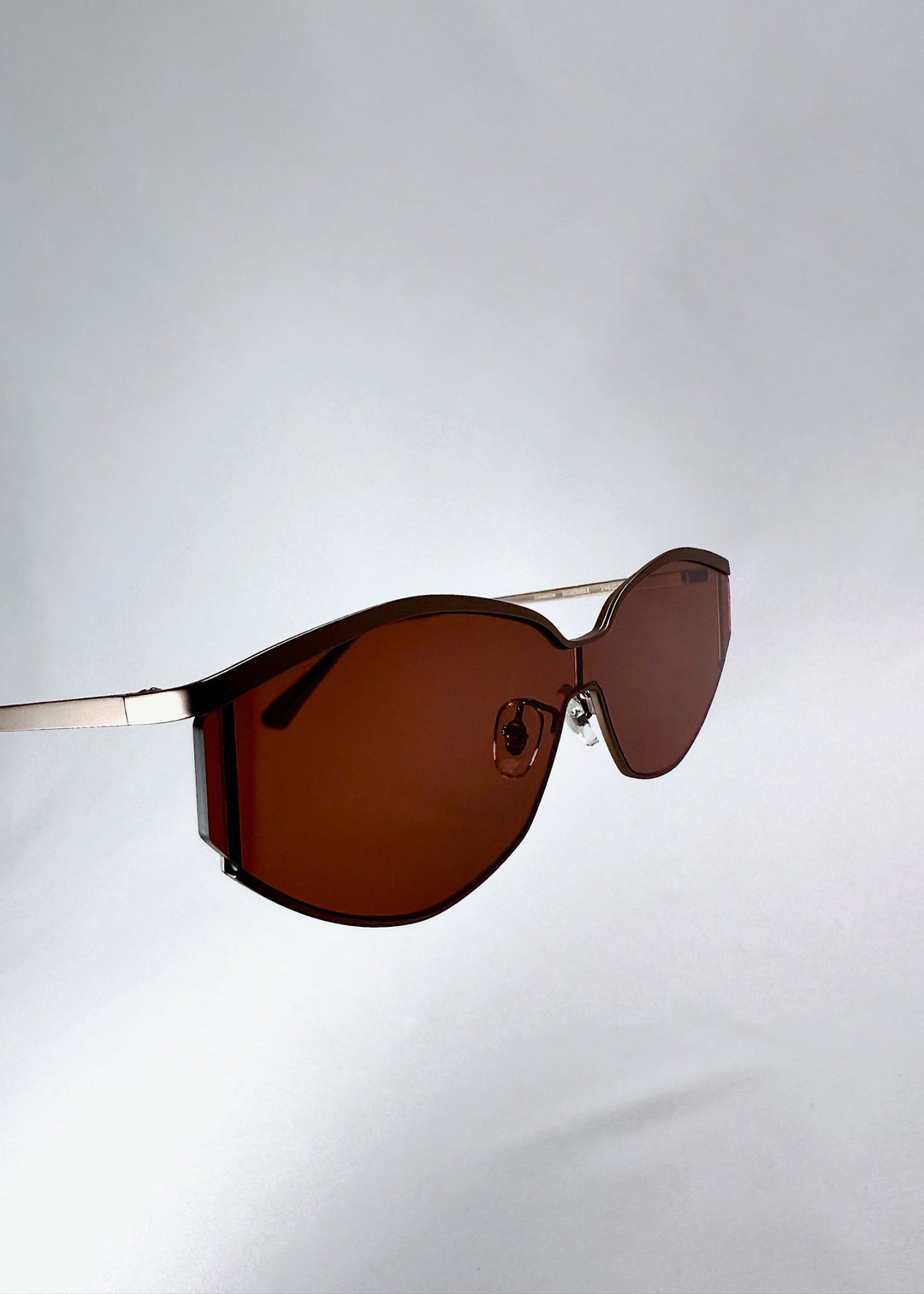 Side profile of Celestia – Ruby Smoke showing the slim champagne-silver metal temples and the rust-red lens edge. 