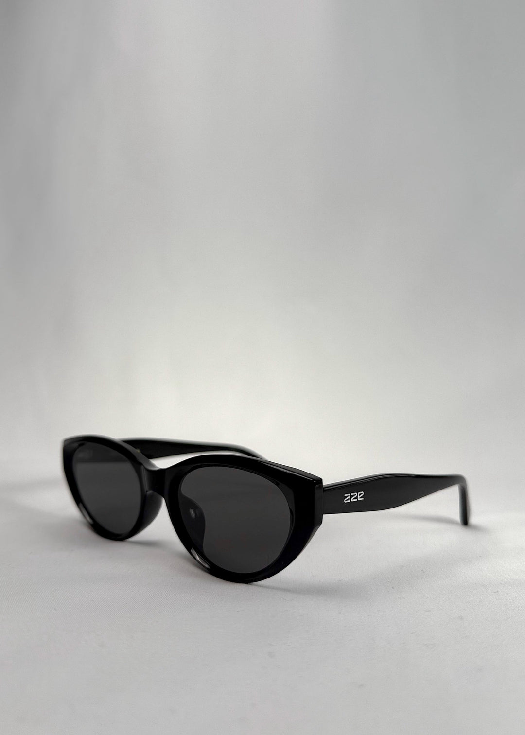 Three-quarter front view of Chara sunglasses in Black, featuring a glossy black cat-eye acetate frame and UV400 lenses, showing the front shape and temple profile. 