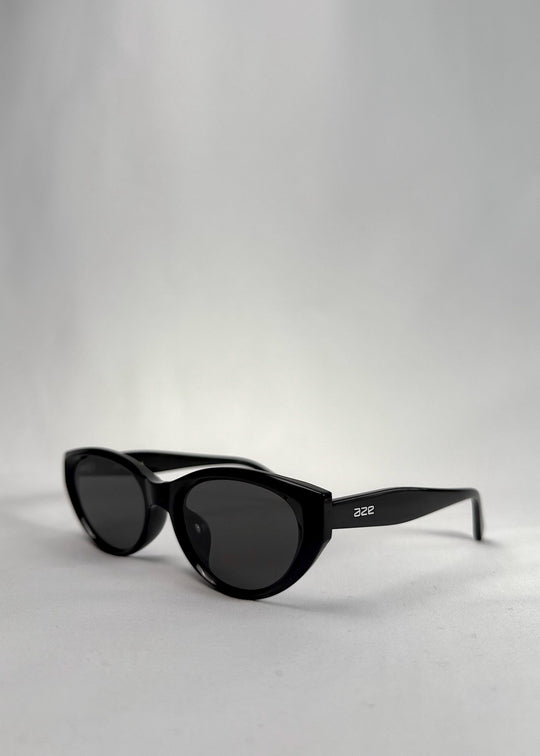 Three-quarter front view of Chara sunglasses in Black, featuring a glossy black cat-eye acetate frame and UV400 lenses, showing the front shape and temple profile. 