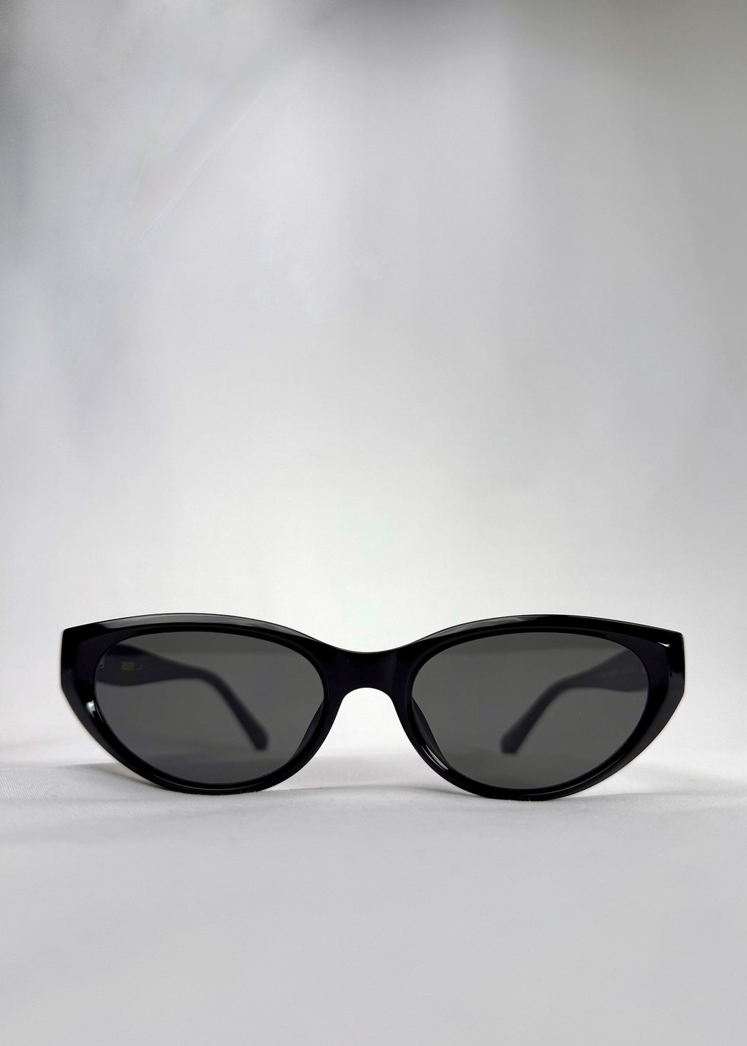 Front view of Chara sunglasses in Black, featuring a glossy black cat-eye acetate frame and UV400 lenses, showing the full front silhouette. 