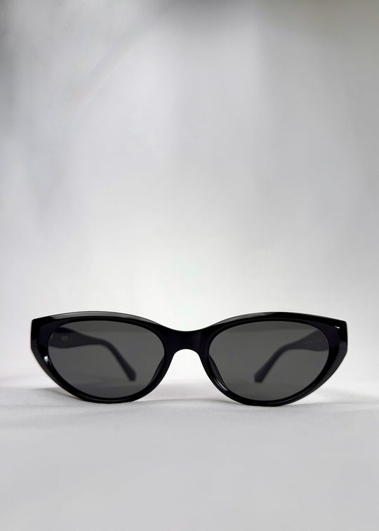 Front view of Chara sunglasses in Black, featuring a glossy black cat-eye acetate frame and UV400 lenses, showing the full front silhouette. 