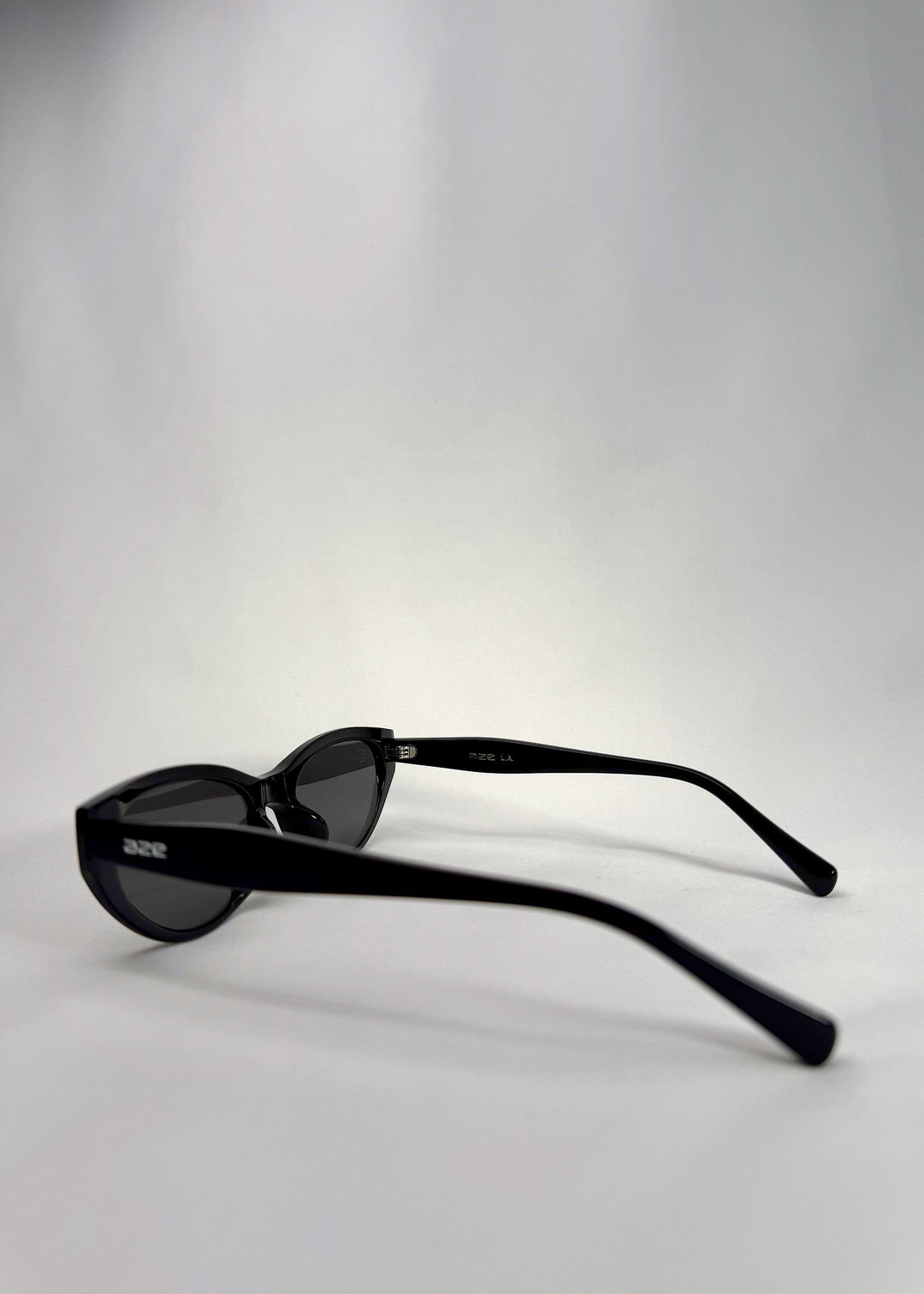 Side-angle view of Chara sunglasses in Black, featuring a glossy black cat-eye acetate frame and UV400 lenses, showing the lens shape and temple profile. 