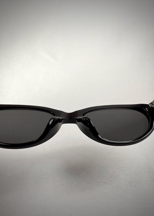 Close-up nose bridge view of Chara sunglasses in Black, featuring a glossy black cat-eye acetate frame and UV400 lenses, showing the bridge and lens edge. 