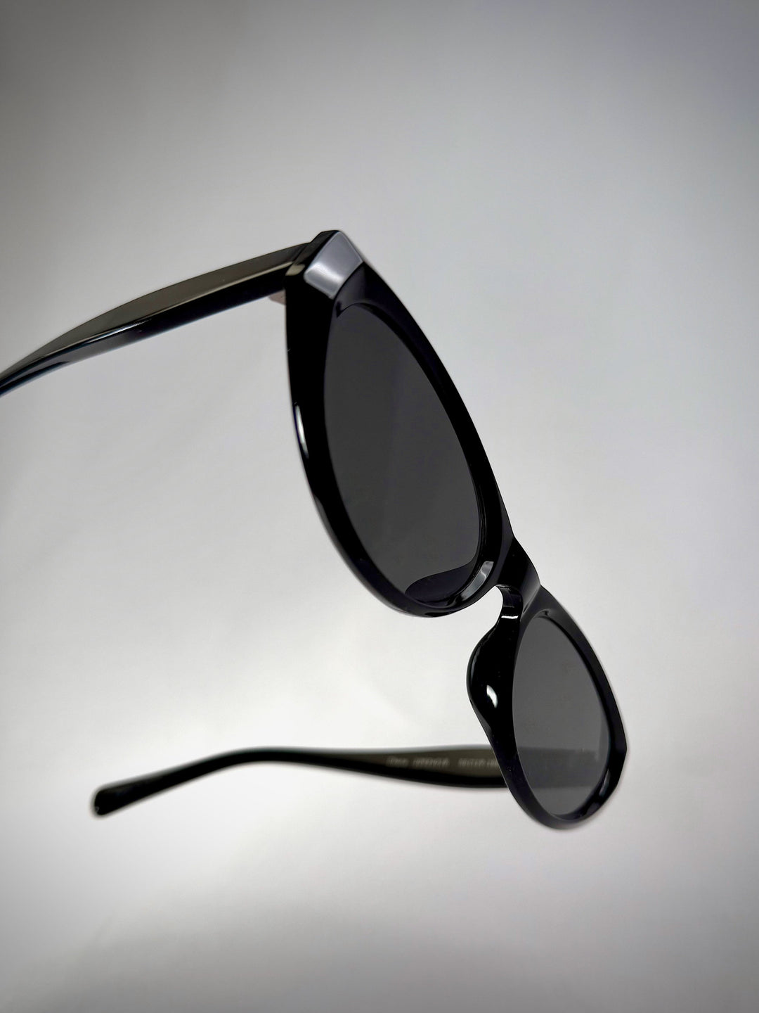 Side view of Chara sunglasses in Black, featuring a glossy black cat-eye acetate frame and UV400 lenses, showing the temple arms and glossy finish. 