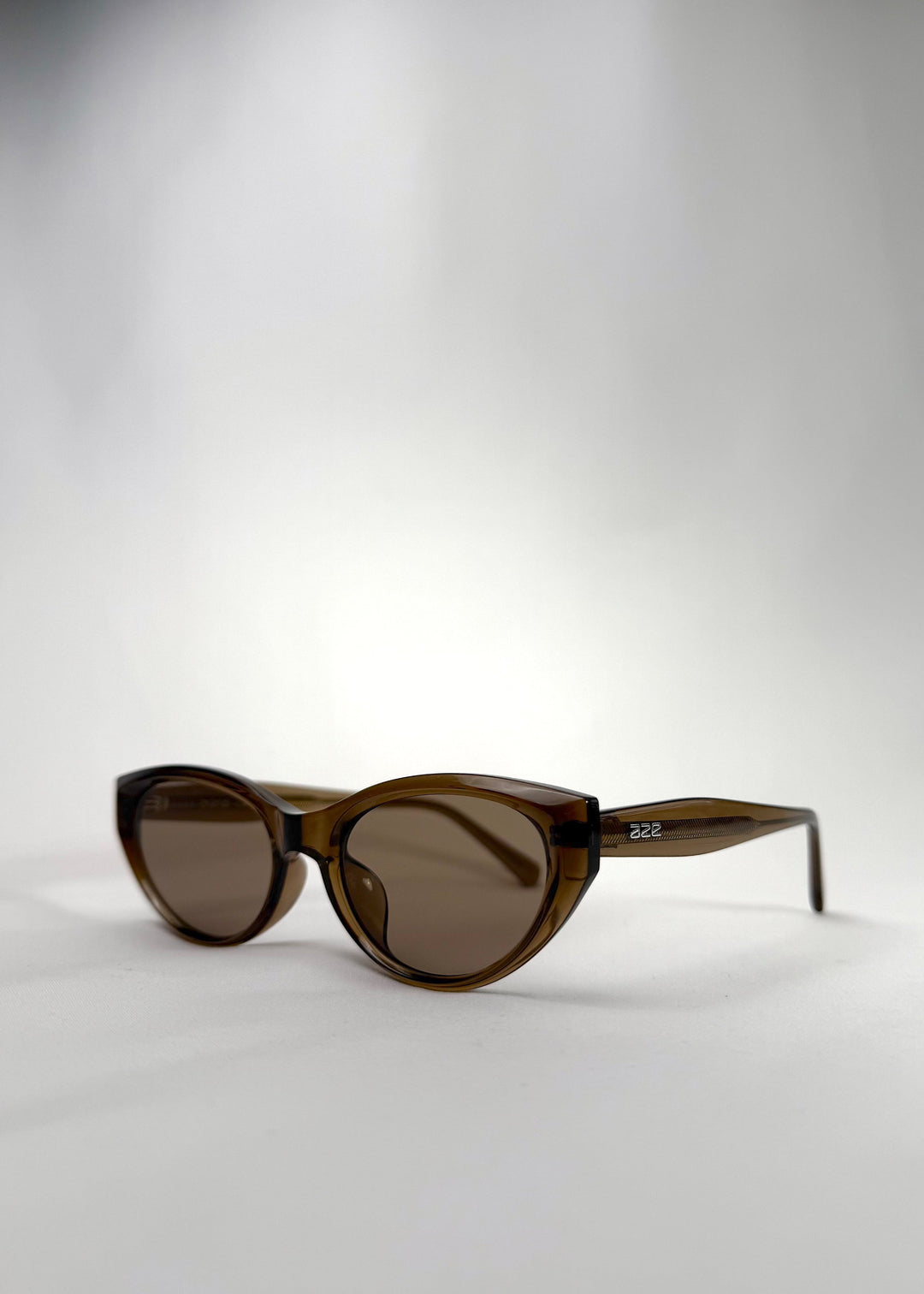 Three-quarter front view of Chara sunglasses in Champagne Brown, featuring a translucent champagne brown cat-eye acetate frame and UV400 lenses, showing the front shape and temple profile. 