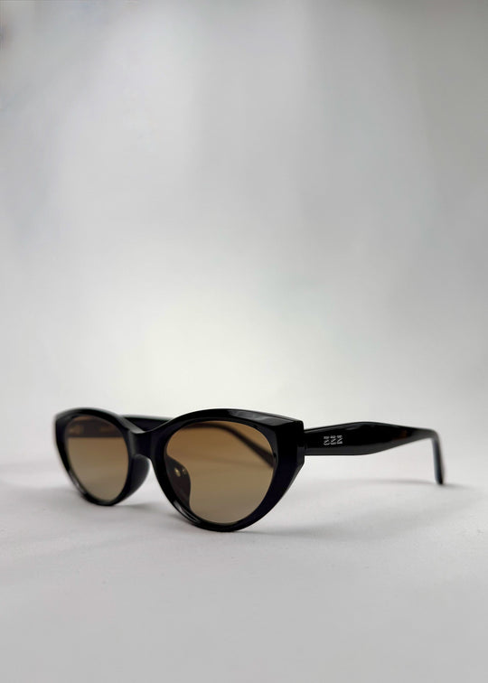 Three-quarter front view of Chara sunglasses in Gradient Amber, featuring a glossy black cat-eye acetate frame with amber gradient lenses, showing the front shape and temple profile. 