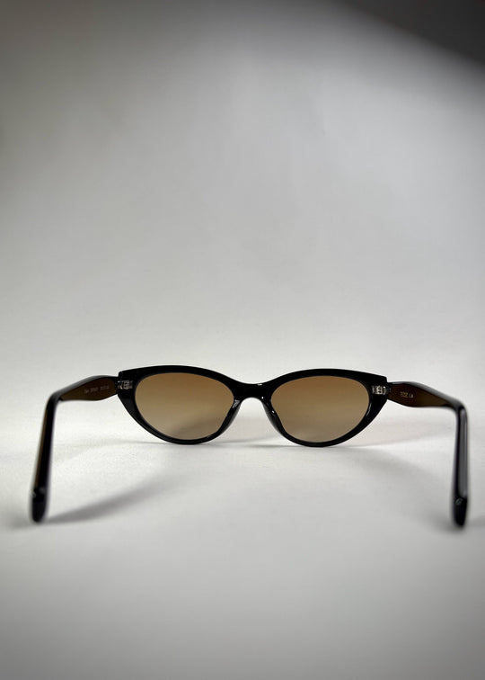 Back view of Chara sunglasses in Gradient Amber, featuring a glossy black cat-eye acetate frame with amber gradient lenses, showing the inside frame and open temples. 