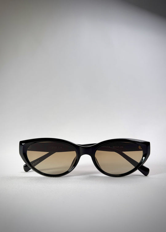 Folded view of Chara sunglasses in Gradient Amber, featuring a glossy black cat-eye acetate frame with amber gradient lenses, showing the folded temples and frame profile. 