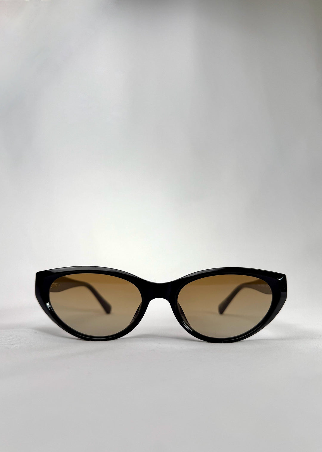 Front view of Chara sunglasses in Gradient Amber, featuring a glossy black cat-eye acetate frame with amber gradient lenses, showing the full front silhouette. 