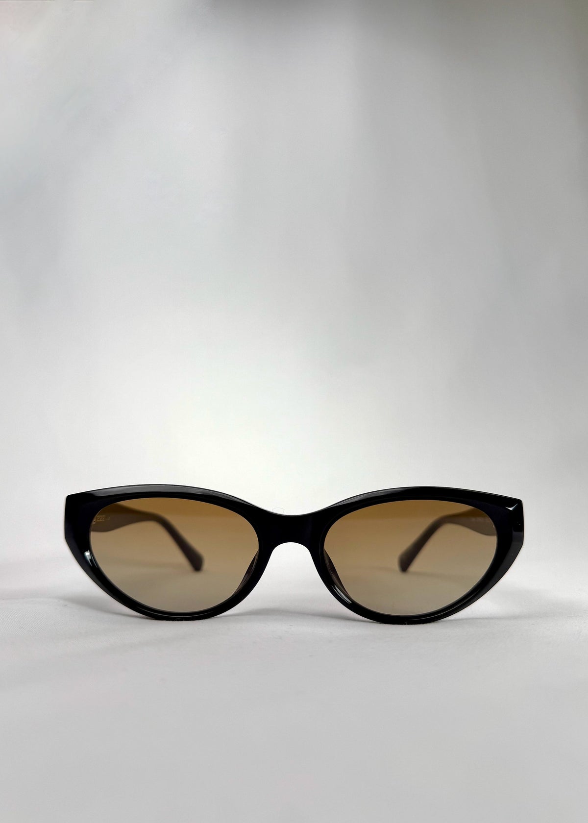 Front view of Chara sunglasses in Gradient Amber, featuring a glossy black cat-eye acetate frame with amber gradient lenses, showing the full front silhouette.