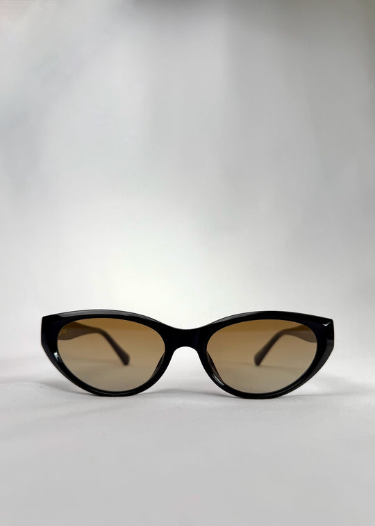 Front view of Chara sunglasses in Gradient Amber, featuring a glossy black cat-eye acetate frame with amber gradient lenses, showing the full front silhouette. 