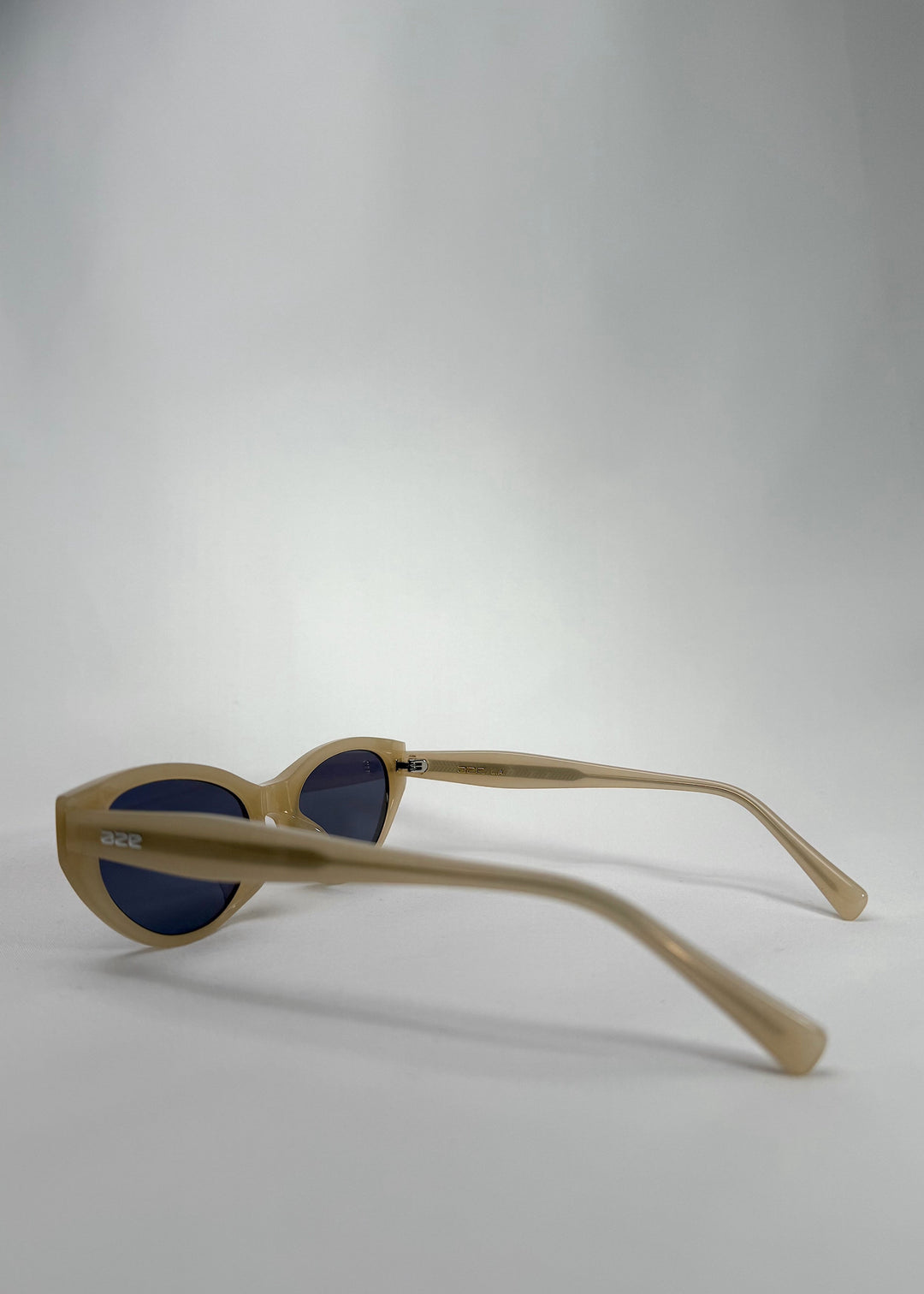 Back-angle view of Chara sunglasses in Milky White, featuring a translucent ivory cat-eye acetate frame and deep blue lenses, showing the temple arms and inside frame. 