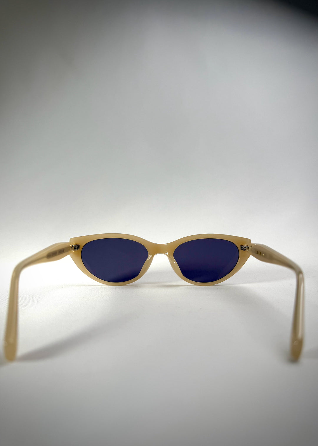 Back view of Chara sunglasses in Milky White, featuring a translucent ivory cat-eye acetate frame and deep blue lenses, showing the inside frame and open temples. 