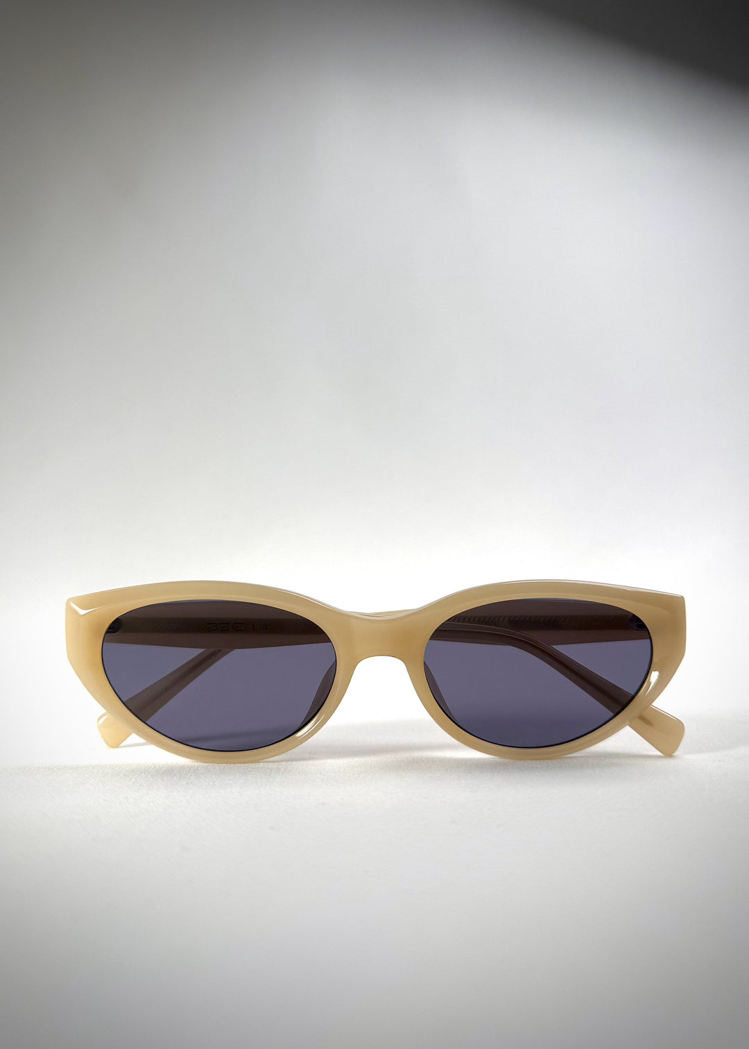 Folded view of Chara sunglasses in Milky White, featuring a translucent ivory cat-eye acetate frame and deep blue lenses, showing the folded temples and frame profile. 