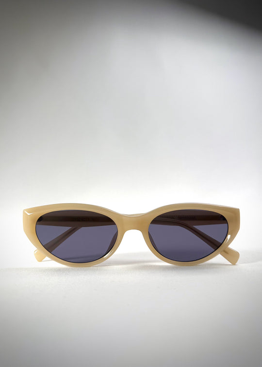 Folded view of Chara sunglasses in Milky White, featuring a translucent ivory cat-eye acetate frame and deep blue lenses, showing the folded temples and frame profile. 