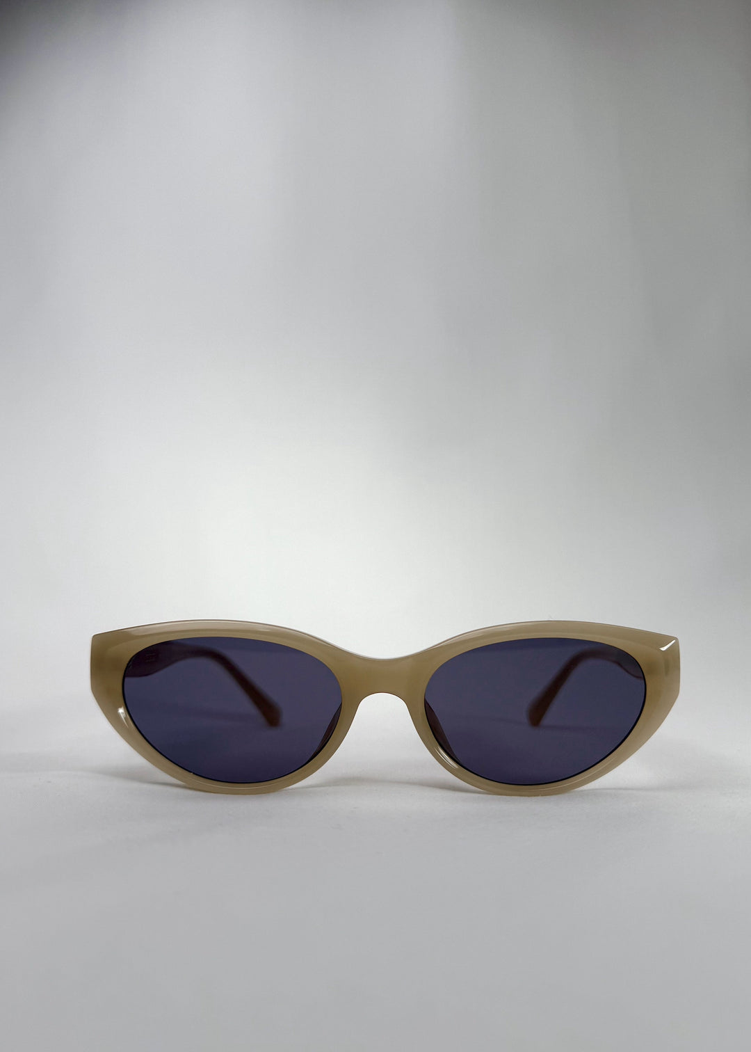 Front view of Chara sunglasses in Milky White, featuring a translucent ivory cat-eye acetate frame and deep blue lenses, showing the full front silhouette. 