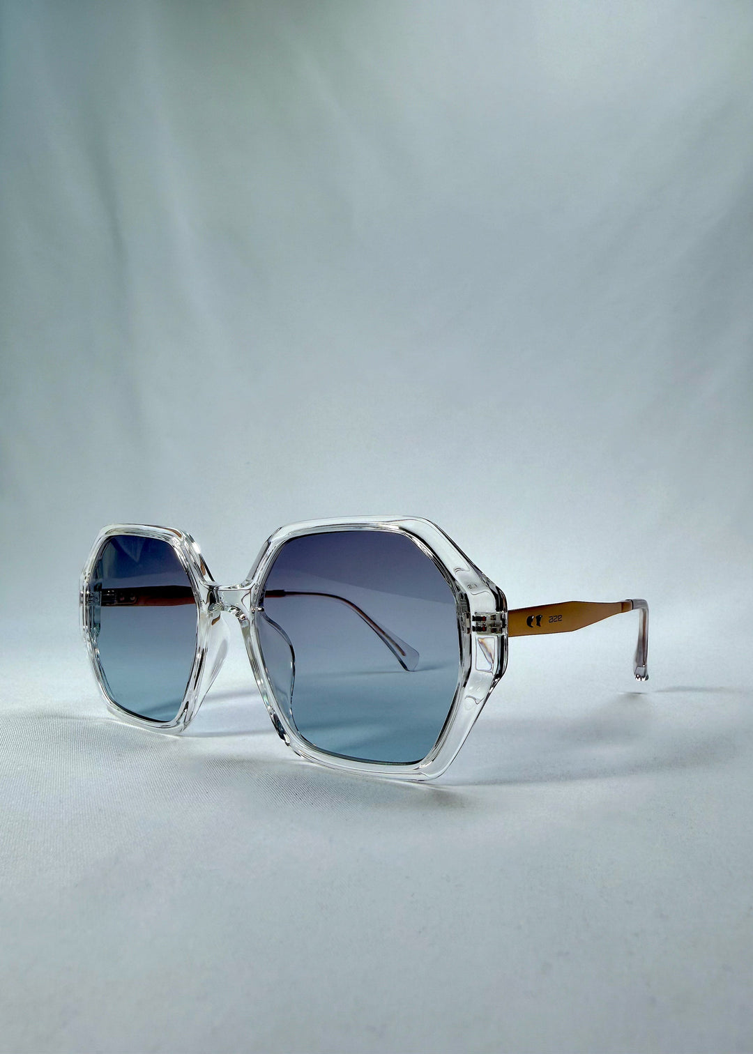 Three-quarter front view of Ciel Arc sunglasses in Glacial Blue, featuring clear frame with blue gradient lenses, showing the front shape and temple profile. 