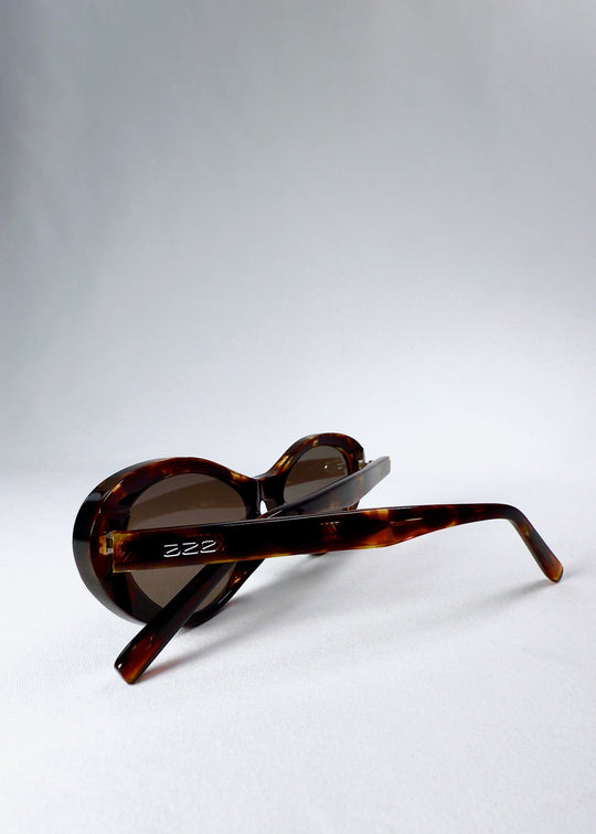 Sunglasses folded with a close view of the tortoiseshell temples and embossed Aze logo (Dagger, Ember Fade). 