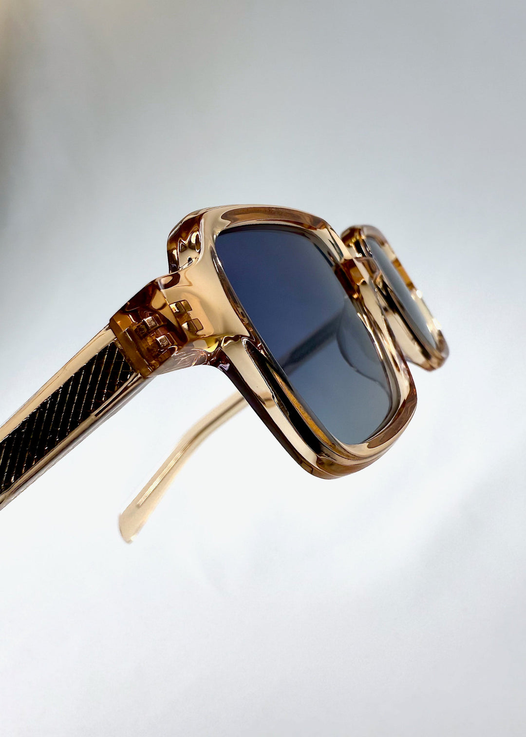 Close-up of the hinge area on Draxen sunglasses in Amber Frost, showcasing the polished acetate finish and textured temple detail. 