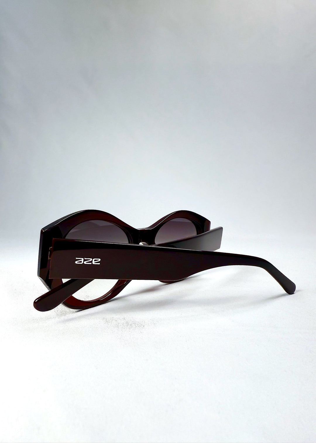 Folded view of Eclipse Feline Crimson Mirage sunglasses, emphasizing the temple design and Aze logo. 