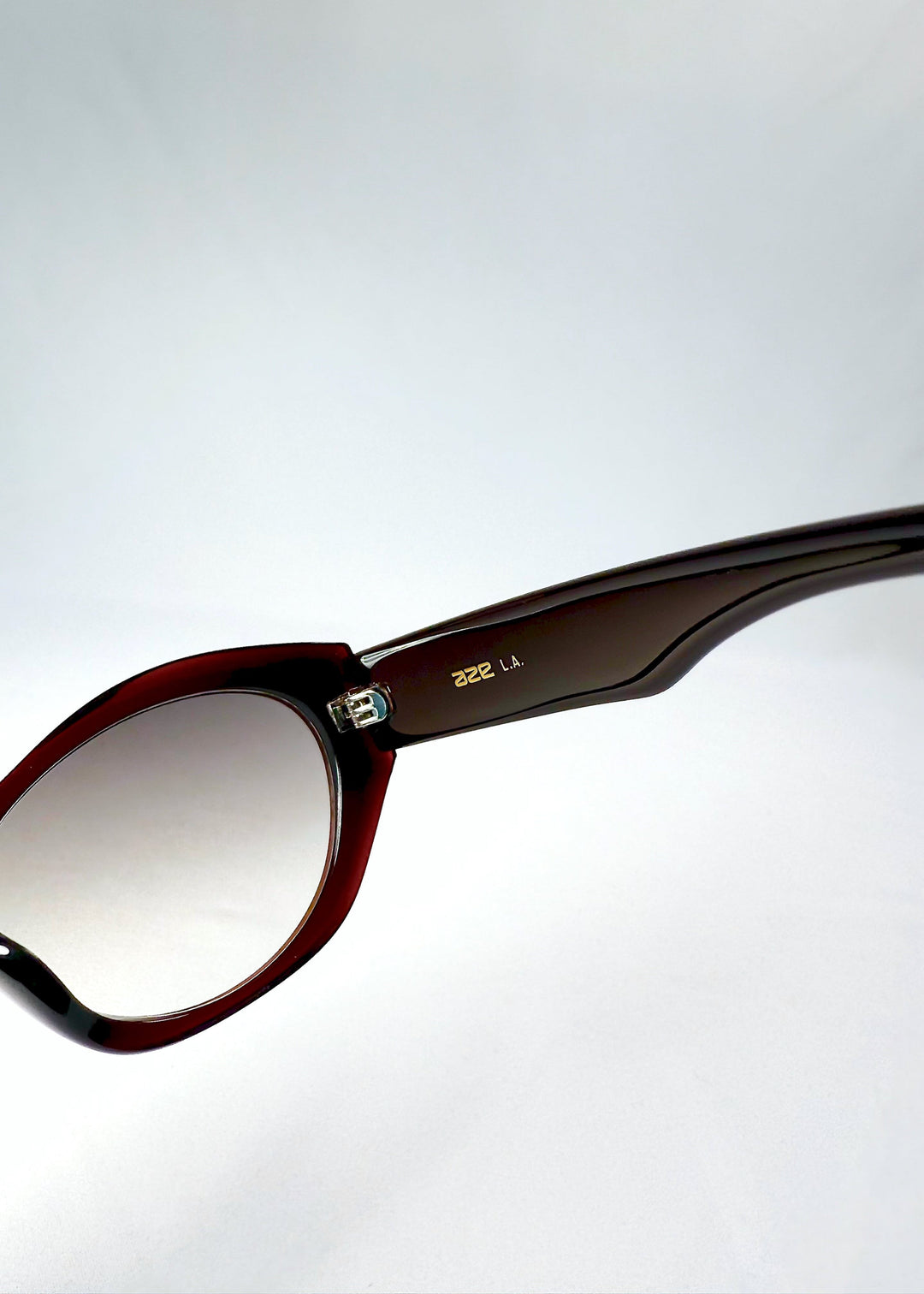 Close-up of the metal hinge and gold AZE L.A. detail on the inner temple of Eclipse Feline Crimson Mirage. 