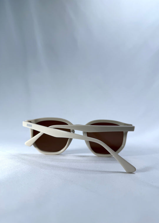 Folded view of Elara sunglasses in Creamy Beige, featuring creamy beige acetate frame and warm brown lenses, showing the folded temples and frame profile. 
