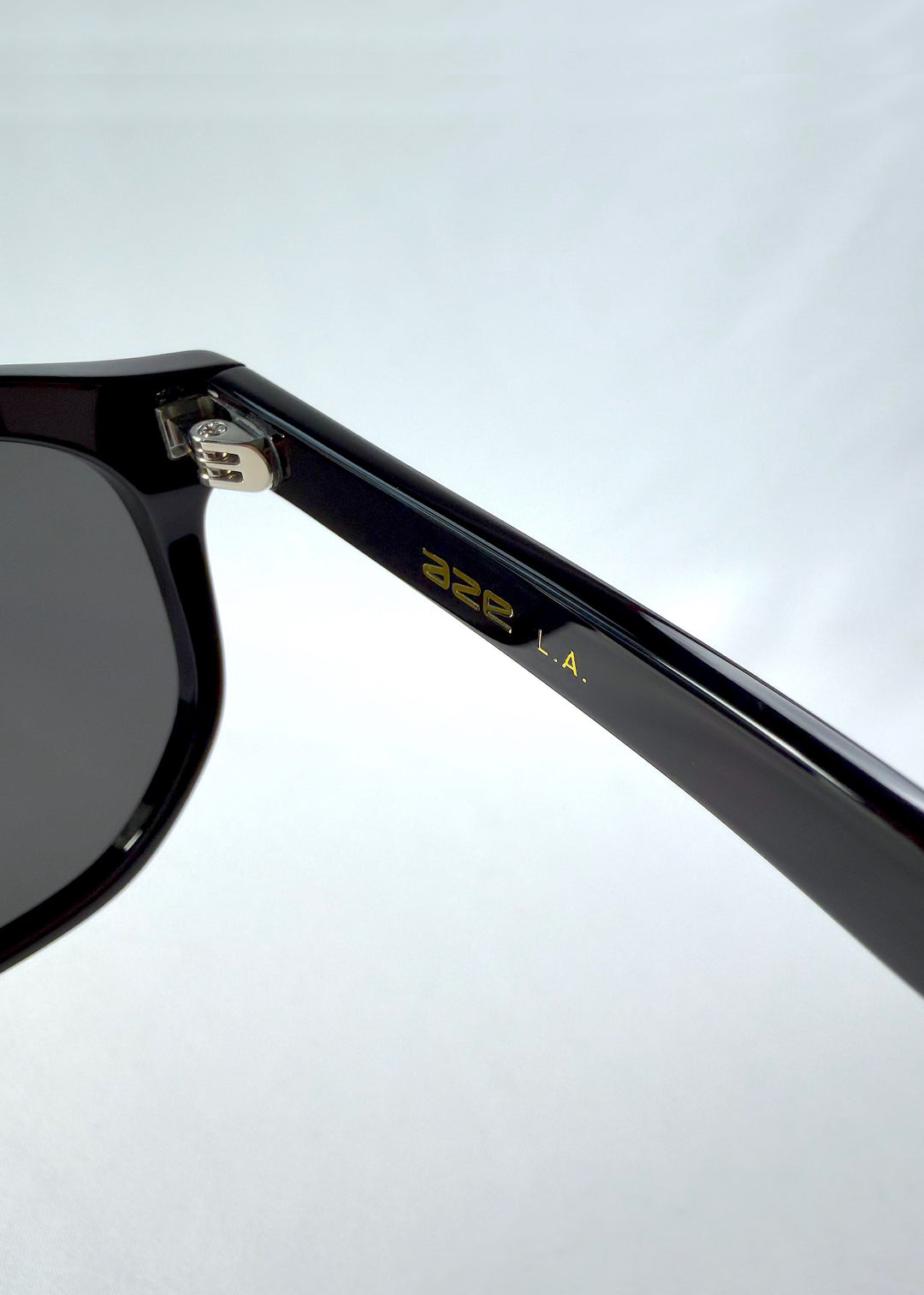 Close-up hinge detail view of Elara sunglasses in Obsidian Black, featuring black acetate frame and dark lenses, showing the hinge, lens edge, and temple detail.