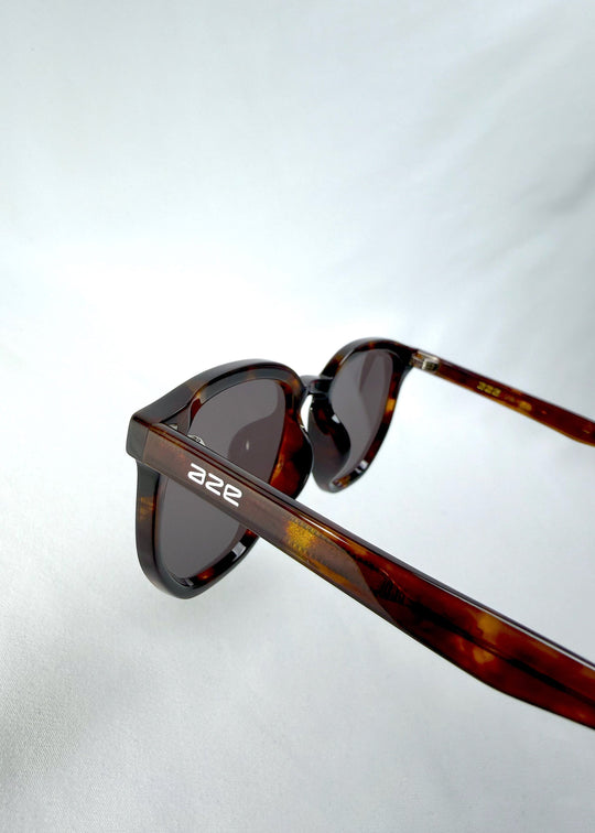 Close-up hinge detail view of Elara sunglasses in Tortoiseshell, featuring tortoiseshell acetate frame and dark lenses, showing the hinge, lens edge, and temple detail. 