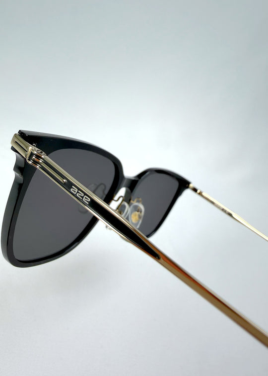 Close-up hinge detail view of Eon Drift sunglasses in Duskgold, featuring a structured black frame, gold-tone accents, and smoky lenses, showing the hinge construction, lens edge, and temple connection.