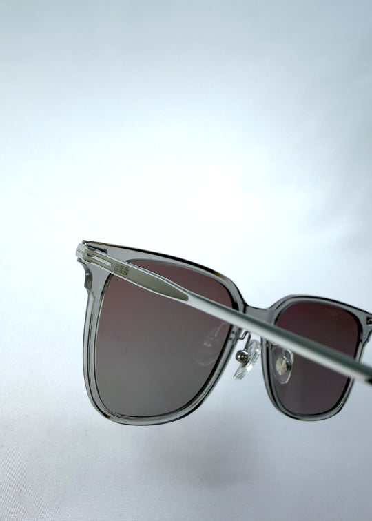 Close-up hinge detail view of Eon Drift sunglasses in Rose Graphite, featuring a rose-gray frame and smoky gradient lenses, showing the hinge construction, lens edge, and temple connection.