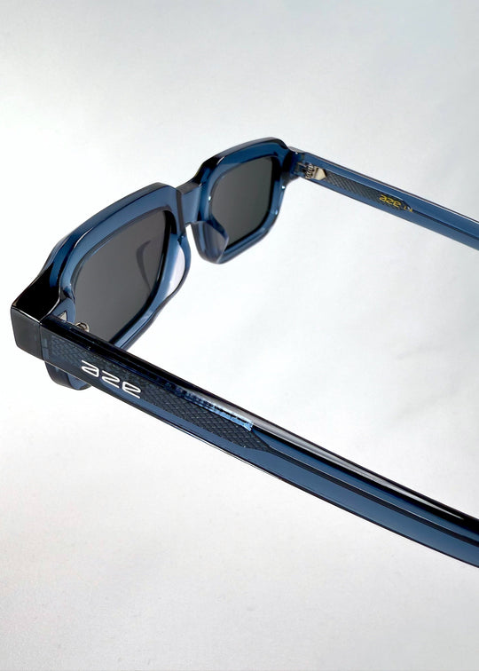 Close-up of Havoc in Abyss Azure highlighting the textured acetate temple and embedded Aze logo on the translucent blue frame. 