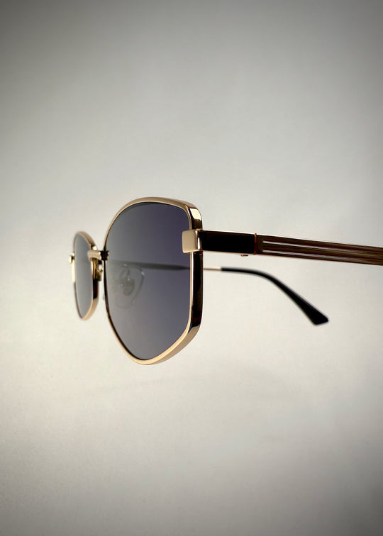 Close-up side view of Sirius B gold stainless steel frame – Premium Prescription Sunglasses featuring intricate temple detailing and blue-gray lenses. 
