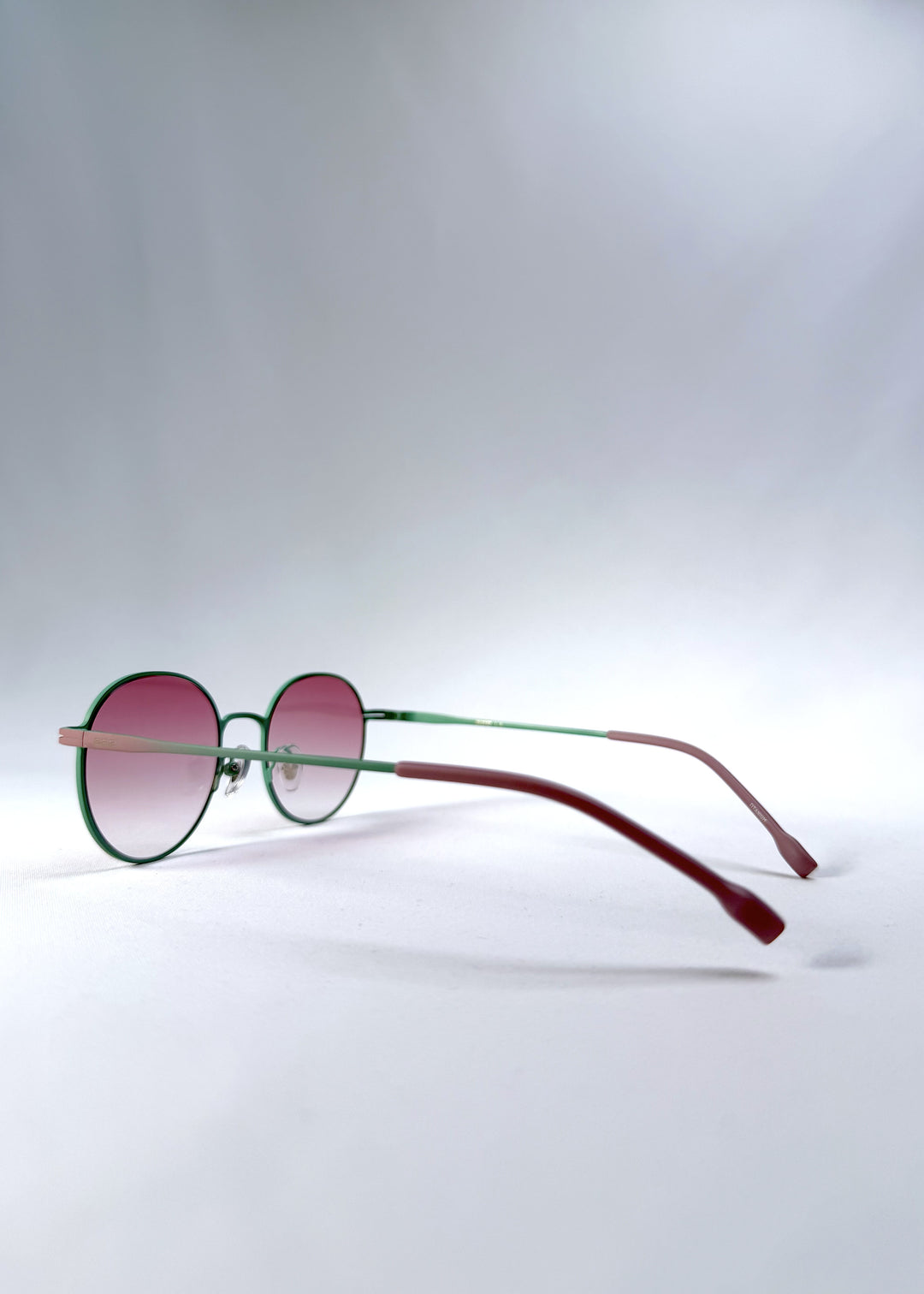 Back-angle view of AZE Liora Arc sunglasses in Mauve Halo, featuring a green-accented round frame and pink gradient lenses, showing the rear frame structure and temple alignment.