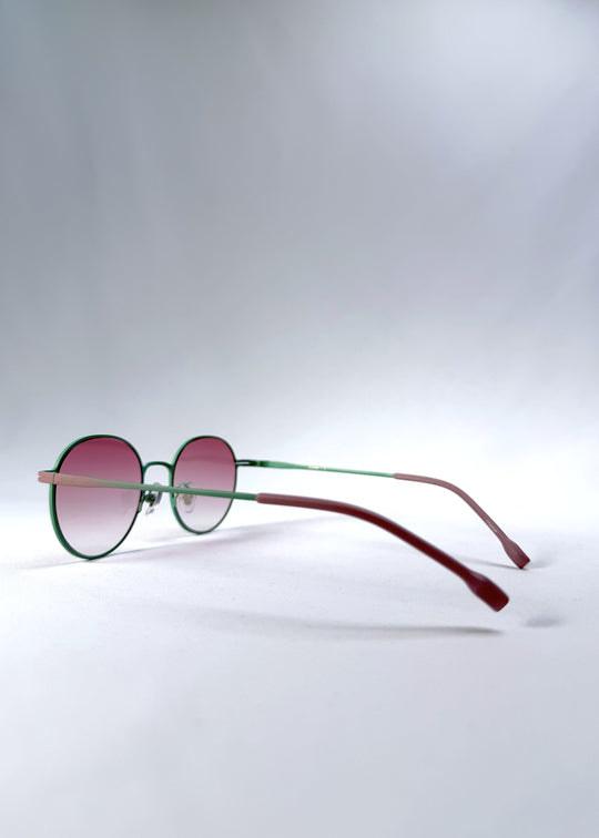 Back-angle view of AZE Liora Arc sunglasses in Mauve Halo, featuring a green-accented round frame and pink gradient lenses, showing the rear frame structure and temple alignment.