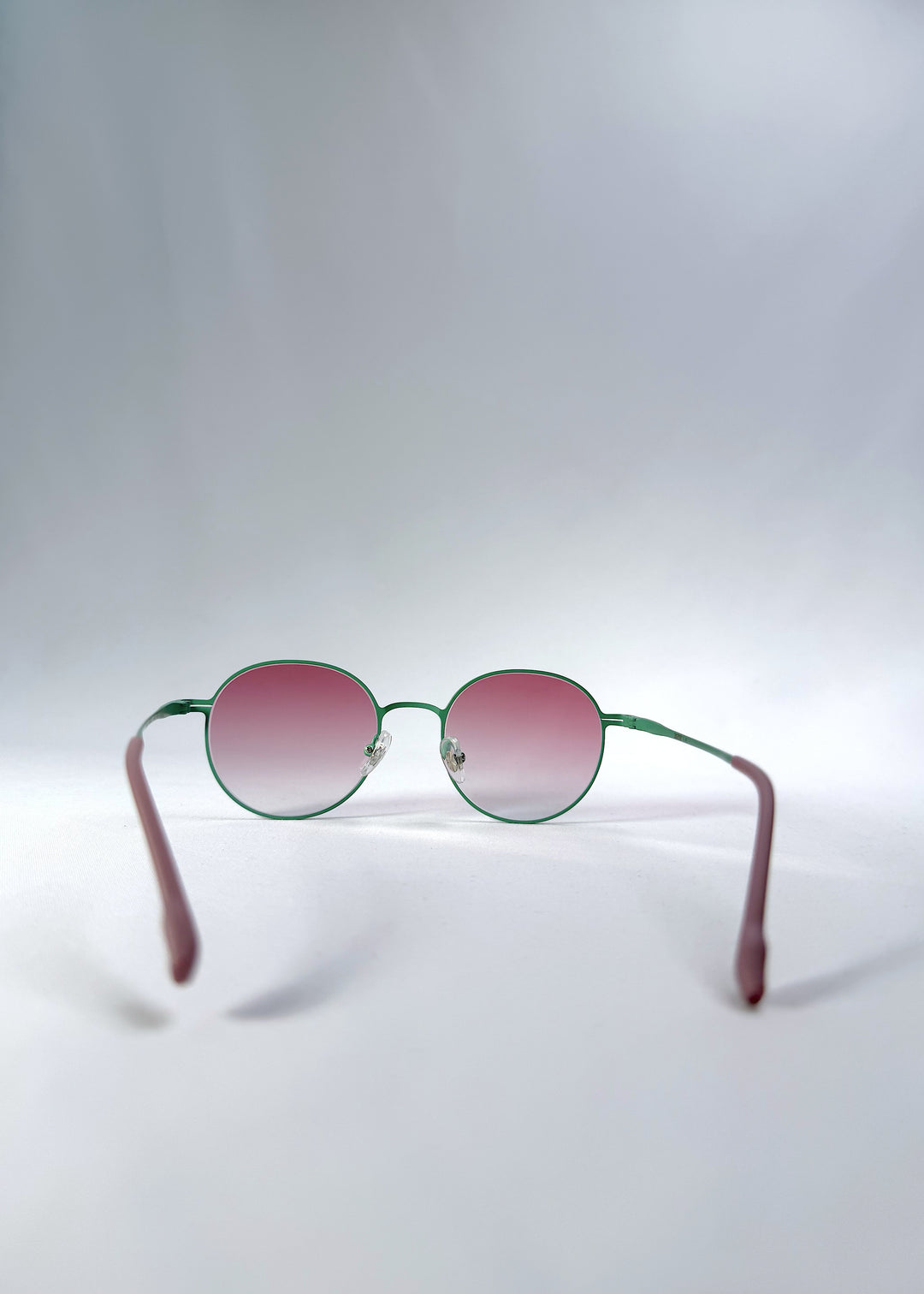 Back view of AZE Liora Arc sunglasses in Mauve Halo, featuring a green-accented round frame and pink gradient lenses, showing the inner frame and open temples.